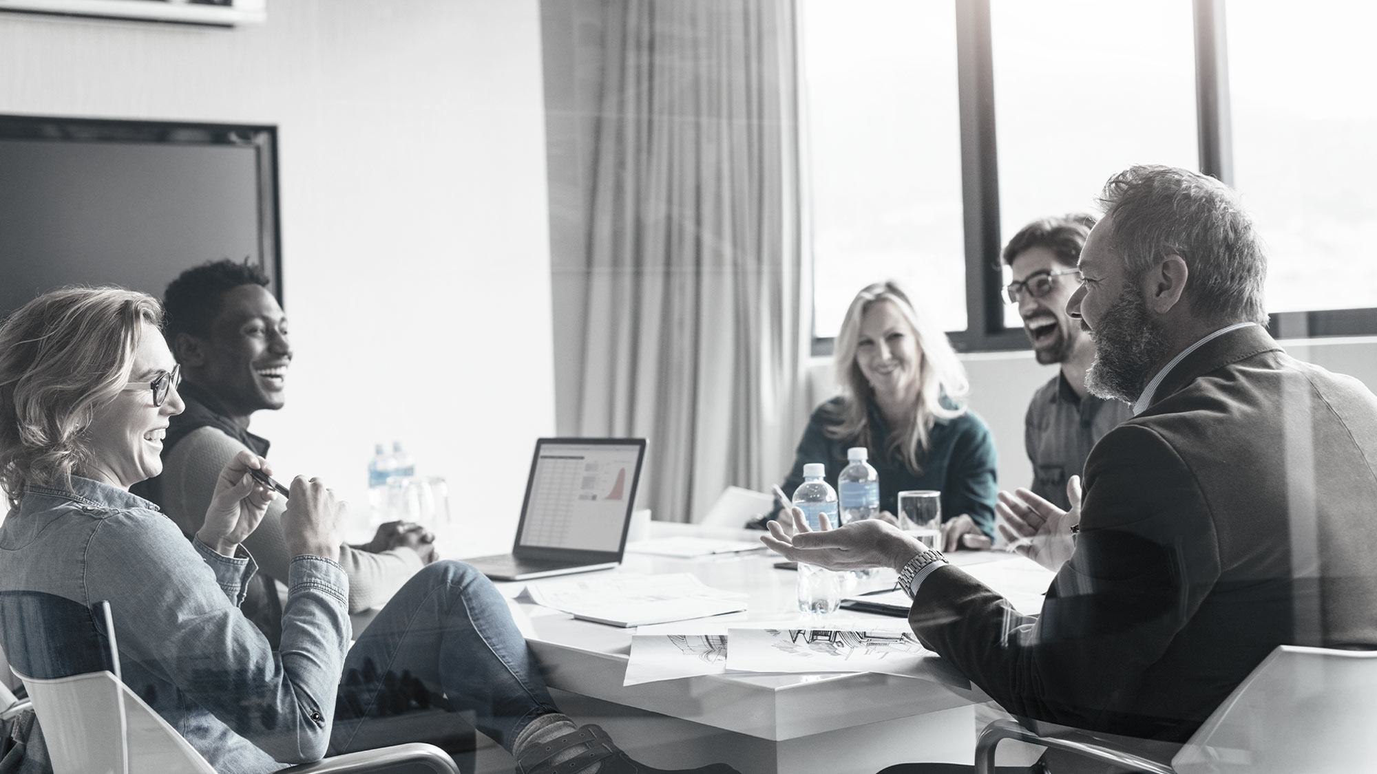 Smiling man and two women talking with an open computer on the desk.